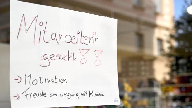 Ein handgeschriebenes Schild „Mitarbeiterin gesucht“ hängt in einem Schaufenster.
