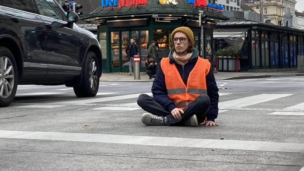 Ein Demonstrant in einer Warnweste sitzt auf einer Straße in Wien.