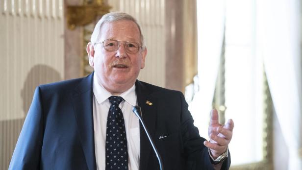 Ein Mann mit Brille und Anzug spricht an einem Mikrofon.