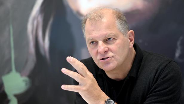 Ein Mann mit einer Armbanduhr gestikuliert vor einem unscharfen Hintergrund.