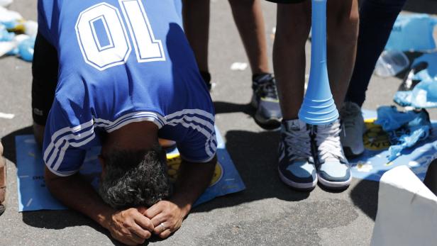 Ein Mann im Argentinien-Trikot kniet auf der Straße, eine Tröte liegt daneben.
