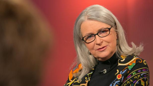 Eine Frau mit grauen Haaren und Brille trägt eine farbenfrohe Jacke.