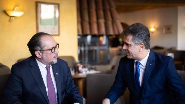 Zwei Männer in Anzügen unterhalten sich in einem Innenraum.