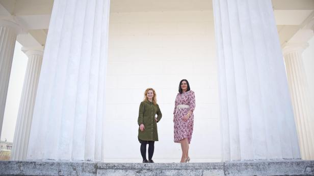 Zwei Frauen posieren vor einem Gebäude mit weißen Säulen.