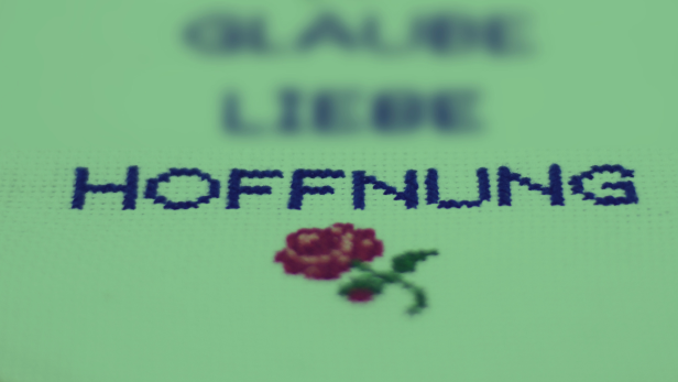 Eine Stickerei mit den Worten Glaube, Liebe, Hoffnung und zwei Rosen.