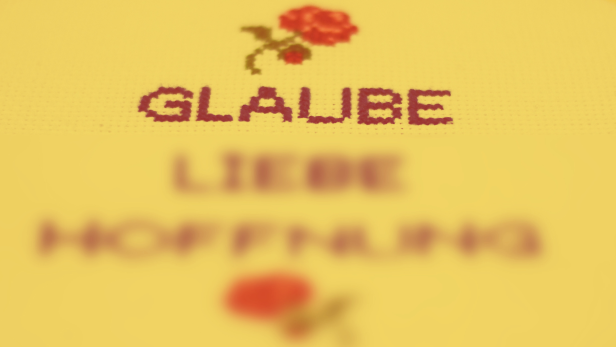 Eine Kreuzsticharbeit mit den Worten „Glaube, Liebe, Hoffnung“ und Rosen.