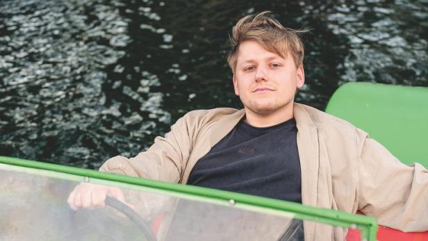 Ein junger Mann steuert ein grünes Motorboot auf dem Wasser.