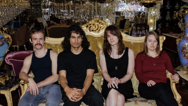 Die Band Liturgy sitzt auf einer goldenen Couch unter einem Kronleuchter.