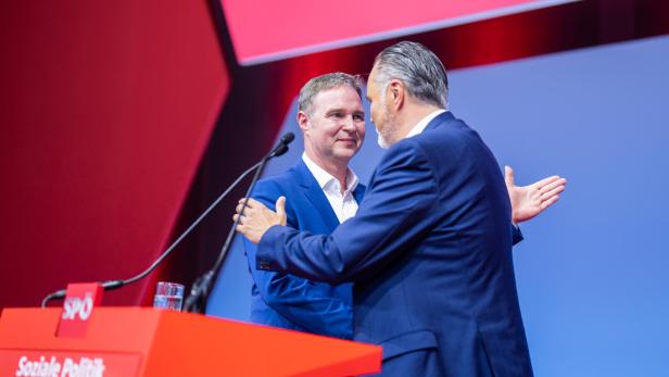 Zwei Männer in Anzügen umarmen sich vor einem Rednerpult der SPÖ.