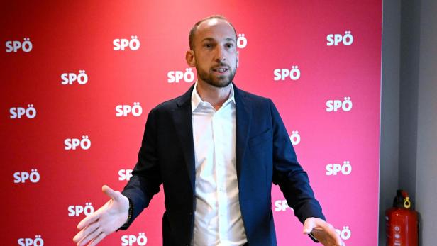 Ein Mann in einem Anzug gestikuliert vor einem roten SPÖ-Hintergrund.