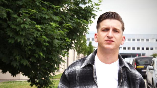 Ein Mann mit Kurzhaarschnitt und karierter Jacke steht im Freien.