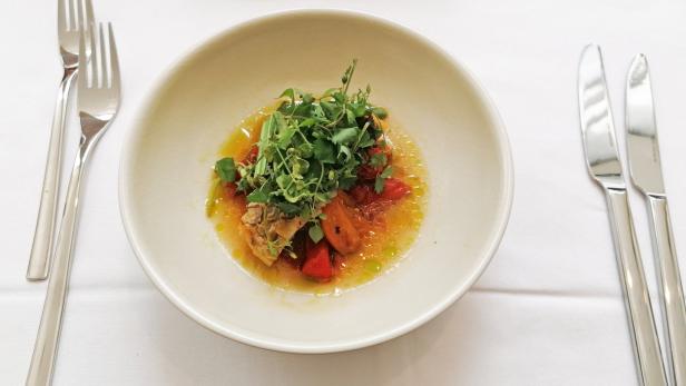 Ein Teller mit Fisch, Tomaten und Kräutern auf einem gedeckten Tisch.