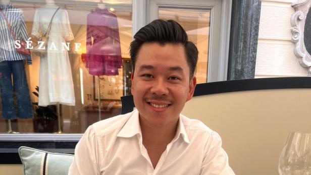 Ein lächelnder Mann sitzt an einem Tisch mit verschiedenen asiatischen Gerichten.