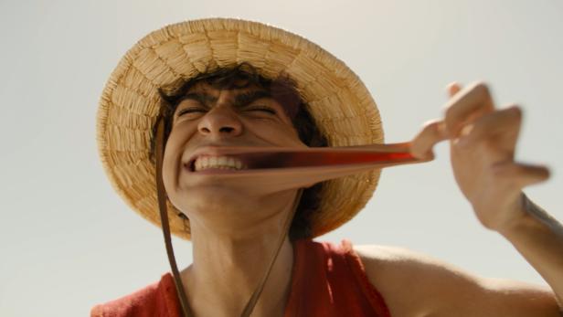 Ein Mann mit Strohhut dehnt sein Gesicht, vermutlich eine Darstellung von Monkey D. Luffy.