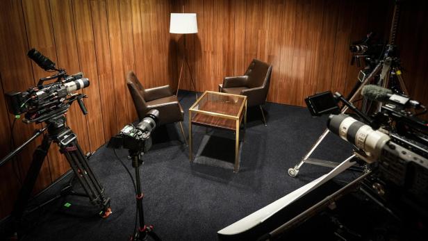 Ein Fernsehstudio mit Kameras, Sesseln und einer Stehlampe.