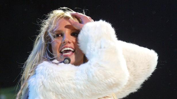 Britney Spears in einem weißen Pelzmantel singt mit einem Mikrofon am Kopf.