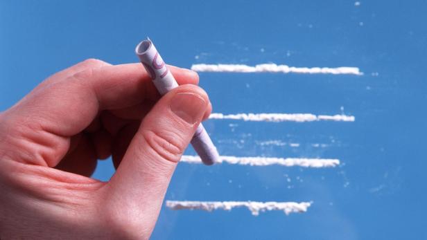 Eine Hand hält eine gerollte Banknote vor Linien aus weißem Pulver.