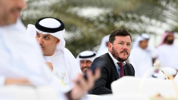 Ein Mann im Anzug sitzt bei einer Veranstaltung mit Männern in traditioneller arabischer Kleidung.