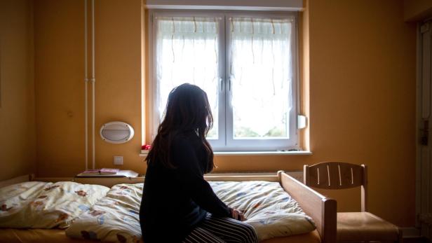 Eine Frau sitzt in einem Frauenhaus auf einem Bett. Frauenhäuser bieten Schutz, wenn der Partner zur Gefahr wird. Dieses Foto stammt von einer Agentur.