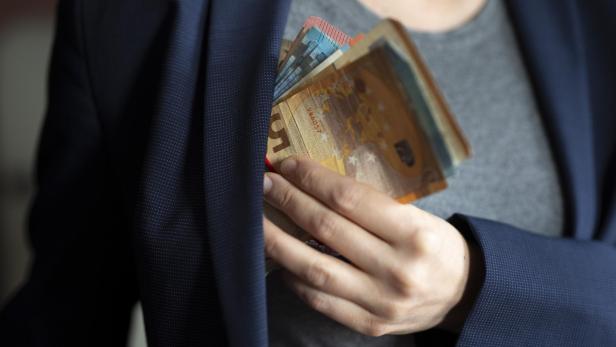 Eine Person steckt einen Stapel Euroscheine in die Innentasche eines blauen Sakkos.