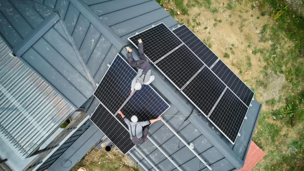 Zwei Arbeiter installieren Solarzellen auf einem grauen Dach.