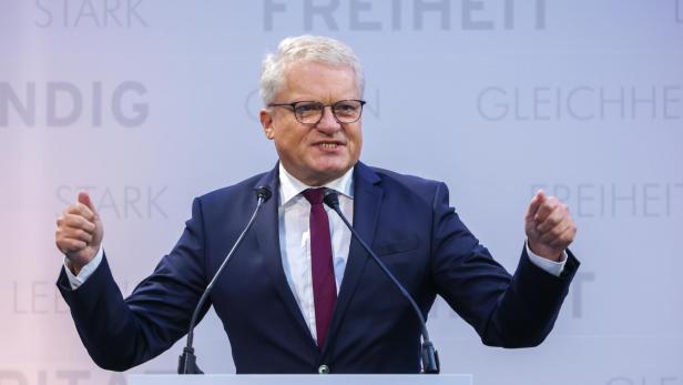 Ein Mann in einem Anzug gestikuliert vor einem Podium mit der Aufschrift „Ein besseres Oberösterreich“.