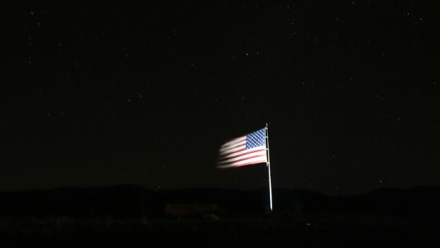 A starry sky is visible as a large U.S. flag waves in the wind along Route 69 in Mayer, Ariz., the night before Americans will vote in the 2024 presidential election, Monday, Nov. 4, 2024. (AP Photo/Julio Cortez)