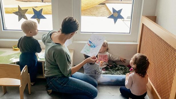 Eine Erzieherin betrachtet mit einer Gruppe von Kindern ein buntes Bild.