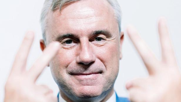 Ein Mann im blauen Sakko zeigt mit beiden Händen das Victory-Zeichen.