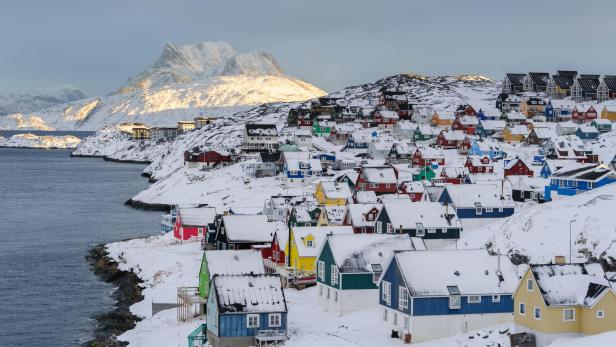 Bunte Häuser bedeckt mit Schnee in einer Küstenstadt mit Bergen im Hintergrund.