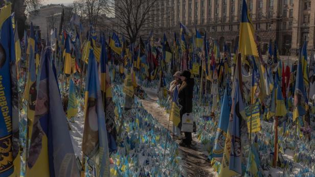 Am 23. Februar 2025, vor dem dritten Jahrestag der russischen Invasion in der Ukraine, stehen Besucher neben einem provisorischen Denkmal, das ukrainische und ausländische Kämpfer mit Fahnen auf dem Unabhängigkeitsplatz in Kiew würdigt.