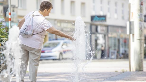 Ein Frau erfrischt sich bei Hitze an einem Brunnen.