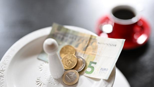 Trinkgeld, Geld und ein Spielstein liegen auf einem Teller, im Hintergrund eine rote Tasse.