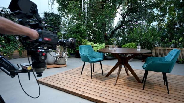 zu sehen ist das Setting der ORF-Sommergespräche 2025: ein großer brauner Tisch und zwei blaue Stühle