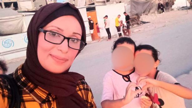 Eine Frau mit Kopftuch auf der Straße vor ihren zwei Kindern mit verpixeltem Gesicht