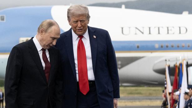 Russlands Präsident Putin und US-Präsident Trump stehen nebeneinander auf einem Flughafen-Rollfeld vor einem Flugzeug, im Hintergrund stehen Soldaten