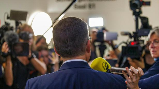 August Wöginger vor Gericht in Linz. August Wöginger ist von hinten zu sehen, vor ihm stehen Reporter mit Kameras und Mikrofonen.