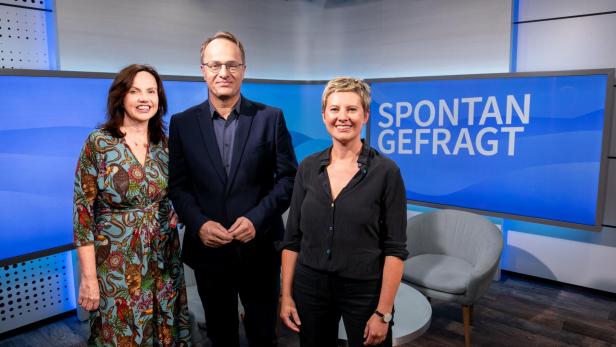 Drei Personen stehen vor einem blauen Bildschirm mit der Aufschrift 'SPONTAN GEFRAGT' in einem Fernsehstudio.
