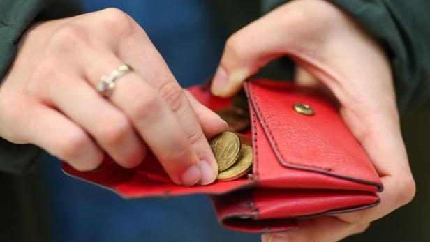 Eine Person öffnet eine rote Geldbörse und nimmt Münzen heraus.