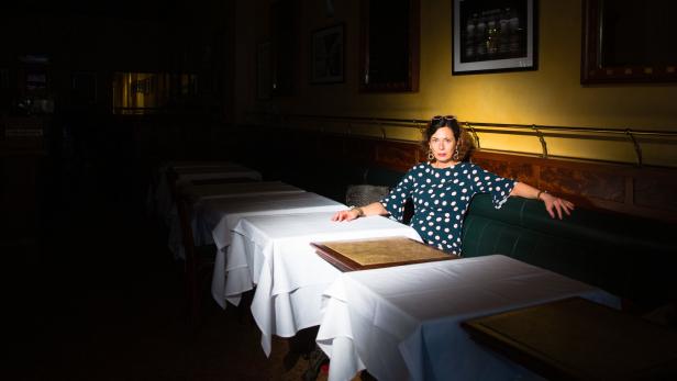 Hell beleuchtete Frau, die an einem Restauranttisch in einem ansonsten ganz abgedunkelten Raum sitzt