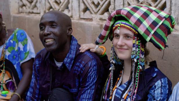 Victoria Preuer und Siaka Touray sind ein Paar. Sie, mit traditionellem Kopfschmuck, legt ihre Hand auf die Schulter des lächelnden Mannes.