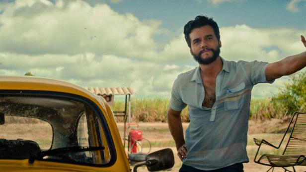 Der Schauspieler Wagner Moura lehnt an einer Säule, neben ihm ein gelbes Auto