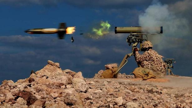 Ein Geschütz schießt eine Rakete ab, ein Soldat hockt unter dem Geschütz.