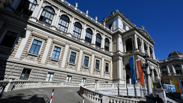 Hauptgebäude der Universität Wien mit bunten Fahnen bei klarem Himmel.