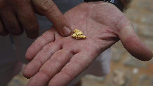 Ein Mann hält ein großes Stück Gold in seiner Hand, er zeigt mit einem Finger darauf.