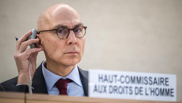 Volker Türk sitzt vor einem Schild ("haut-Commissaire aux droits de l'homme"), er hält sich ein Gerät ans Ohr und blickt in die Kamera.