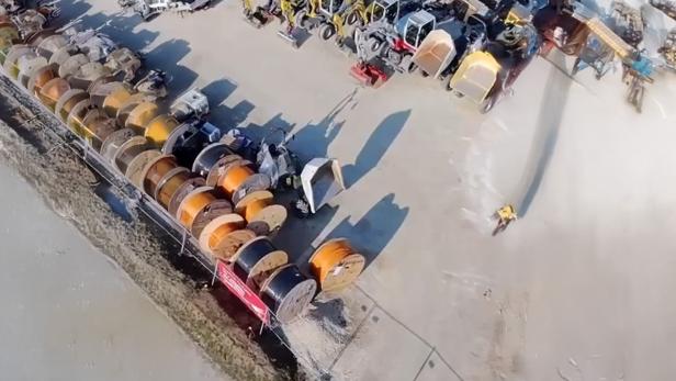 Große Kabeltrommeln und Baumaschinen auf einem Baustellenlagerplatz aus der Vogelperspektive.