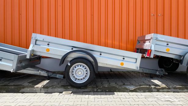Mehrere Autoanhänger stehen vor einem orangen Container.