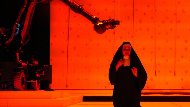 Szenenbild aus "Sancta": eine Nonne kniet in rotem LIcht auf der Bühne, hinter ihr ein Kamera-Kran
