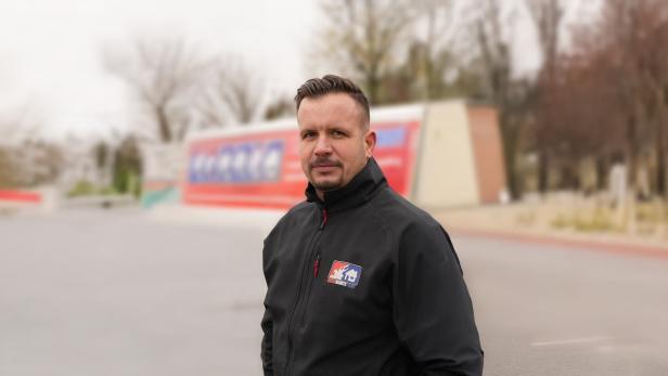 Mann in schwarzer Jacke mit Brandschutz-Logo steht im Freien vor unscharfem Hintergrund.